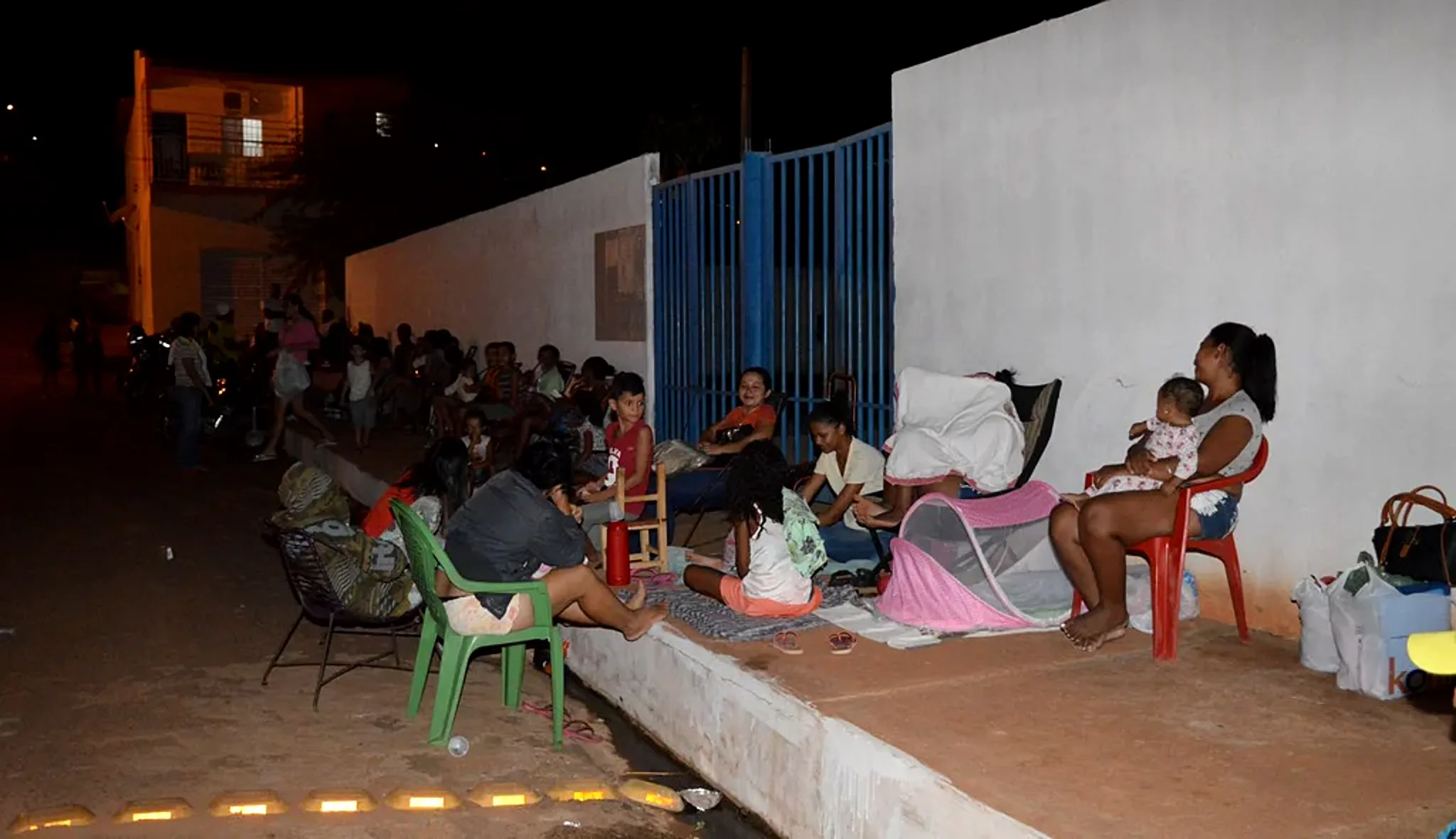 Famílias aguardando à noite em frente a uma escola municipal